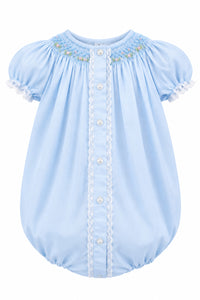 A light blue baby romper with short puff sleeves, a button-down front, lace trim, and delicate floral embroidery at the neckline, hanging on a white hanger against a neutral gray background.