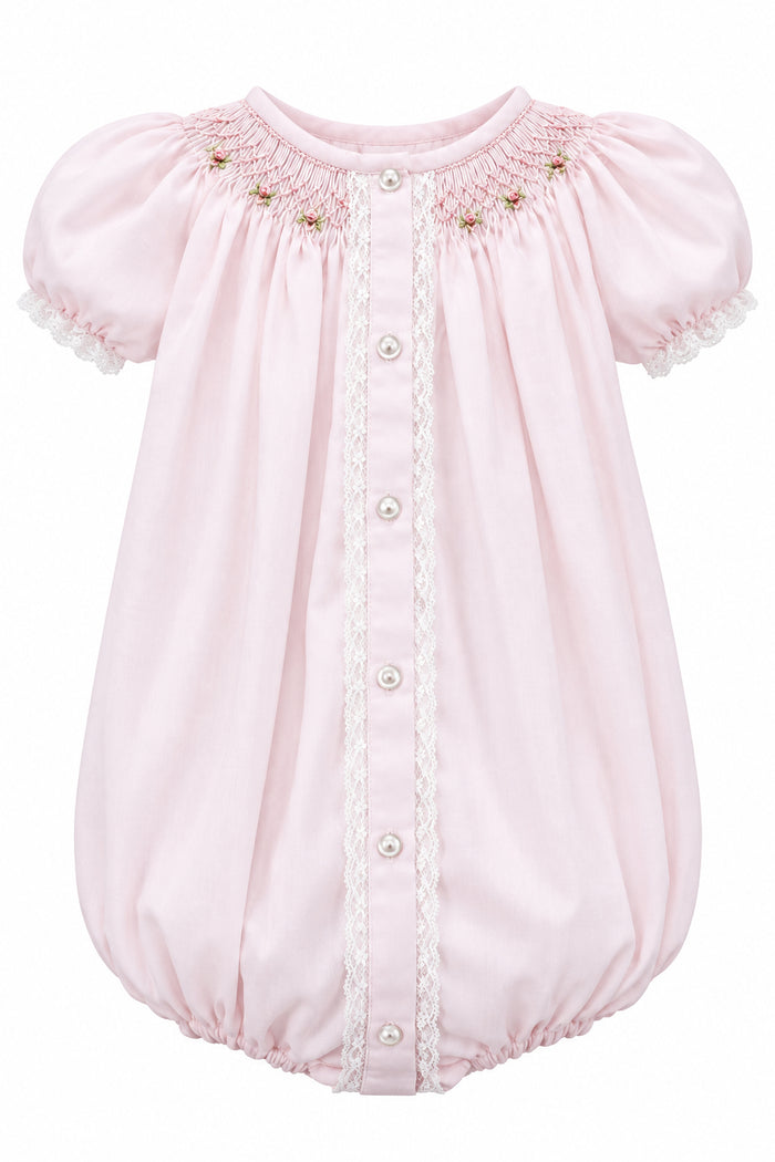 A light pink baby smocked bodysuit with short puff sleeves, lace trim, and a snap-button front, hanging on a white hanger against a neutral gray background.