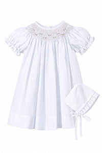 White baby dress with lace details on a gray background, accompanied by a matching bonnet.