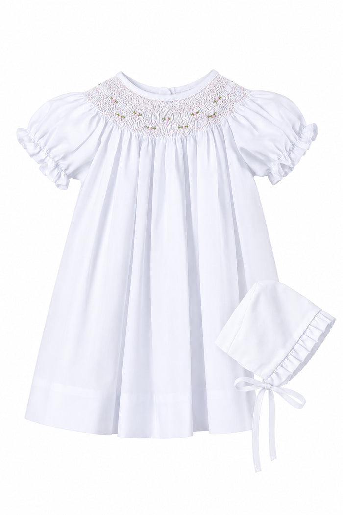 White baby dress with lace details on a gray background, accompanied by a matching bonnet.