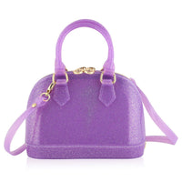 A small dome-shaped purple glitter handbag with gold-tone hardware, dual top handles, and a detachable shoulder strap, shown on a plain white background.