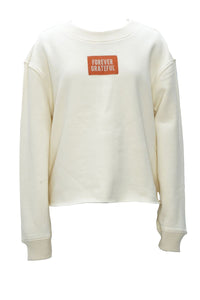 An off-white long-sleeve crewneck sweatshirt featuring a small orange rectangular patch on the chest with the text 'FOREVER GRATEFUL' in white.