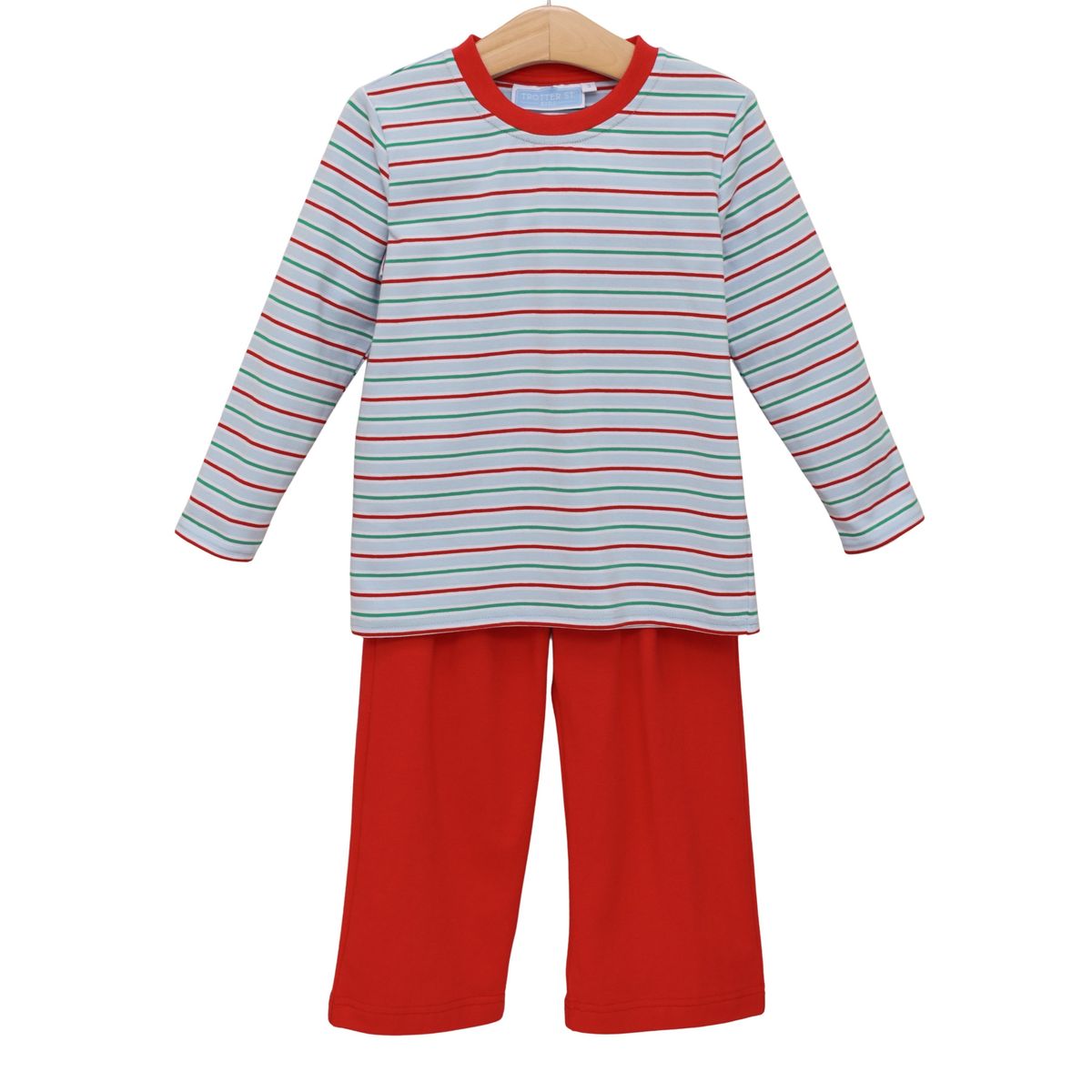 A two-piece children's pajama set on a wooden hanger, featuring a long-sleeve top with thin red and dark blue horizontal stripes on a white background, and solid red pants.