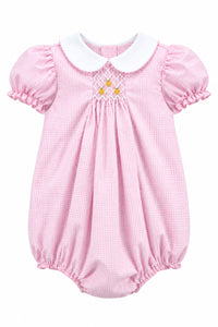 A pink and white gingham baby romper with a white Peter Pan collar, short ruffled sleeves, and a smocked chest detail with three yellow buttons, shown on a hanger against a solid gray background.