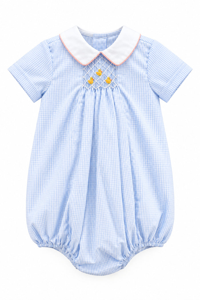 A baby boy's short-sleeve romper in a light blue and white gingham pattern, featuring a white collar with a thin orange trim, smocked detailing at the chest with three small yellow flowers, and elasticated leg cuffs.