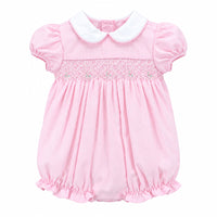 A baby girl's pink bubble romper with a white Peter Pan collar and delicate lace smocking across the chest, hanging on a white hanger against a solid gray background.