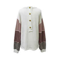 A ribbed knit long-sleeve sweater displayed on a mannequin torso against a plain light gray background. The sweater is primarily off-white with color-blocked sleeves featuring dusty rose, mauve, and gray vertical panels, finished with four decorative buttons at the front neckline.