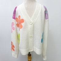 An off-white knit cardigan sweater with colorful floral patches on the sleeves and shoulders, displayed on a mannequin torso against a plain light gray background.