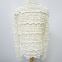 An off-white textured knit sweater with horizontal ruffled tiers, displayed on a dress form against a light gray background.