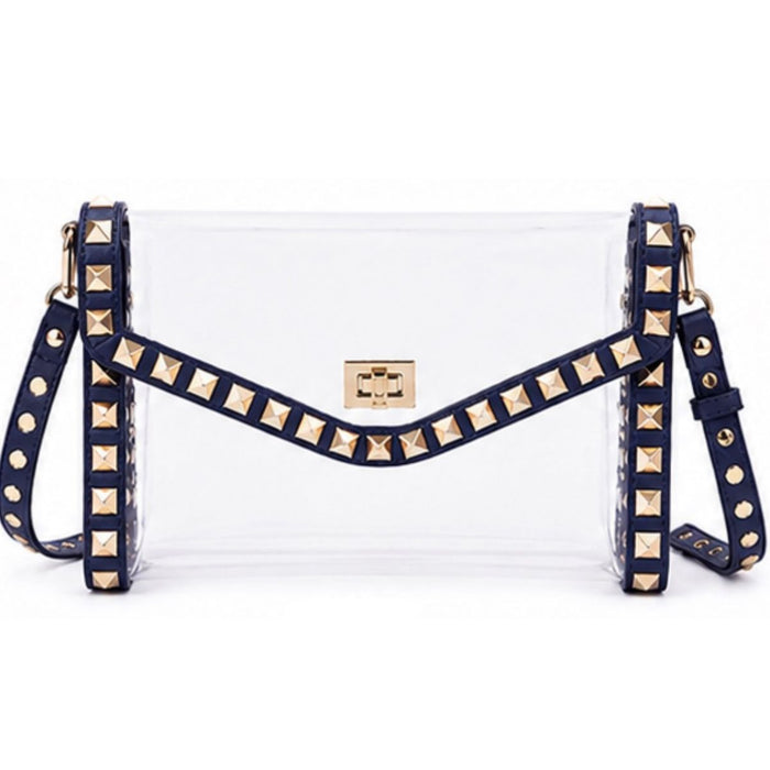 A clear plastic clutch bag with navy blue faux-leather trim and gold pyramid studs, featuring a gold-tone metal logo plate on the front.