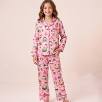 A young girl modeling a two-piece pink pajama set with a cute cartoon animal print, standing against a solid pale pink studio background.