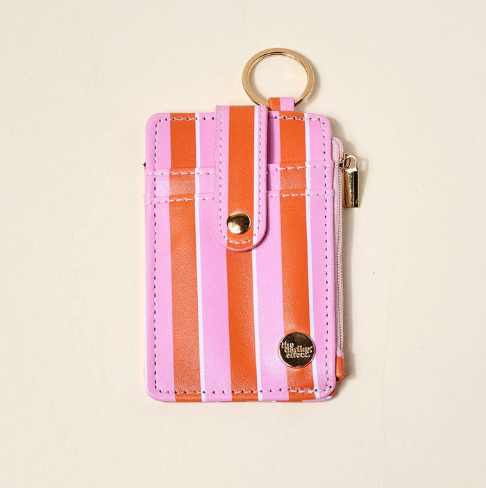 A pink and orange striped faux-leather card holder wallet with a gold-tone key ring, snap button closure, and zippered pocket, shown on a light beige background.