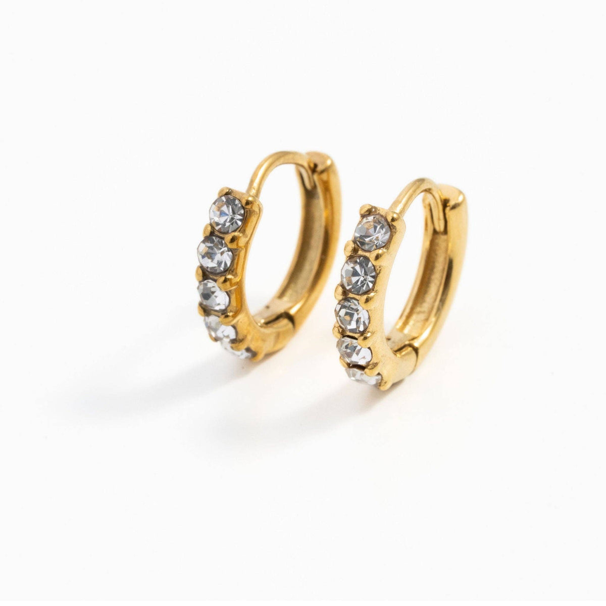 A pair of gold huggie hoop earrings with a row of clear rhinestones on the front, displayed on a clean white background.