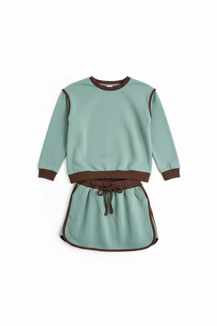 A two-piece children's outfit set featuring a sage green sweatshirt and matching mini skirt with contrasting brown trim, cuffs, and waistband.