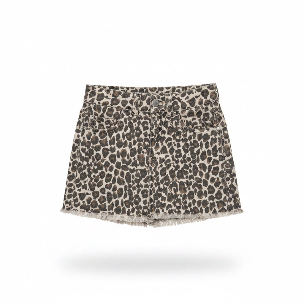 A leopard print denim mini skirt with a frayed hem, held up on a clear plastic hanger by a hand with blue nail polish in a retail store setting.
