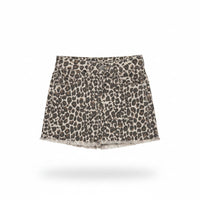 A leopard print denim mini skirt with a frayed hem, held up on a clear plastic hanger by a hand with blue nail polish in a retail store setting.
