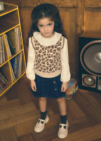 Young girl wearing a leopard print vest and headphones in a room with wooden walls and a bookshelf.