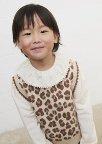 Child wearing a leopard print vest over a white shirt against a plain background