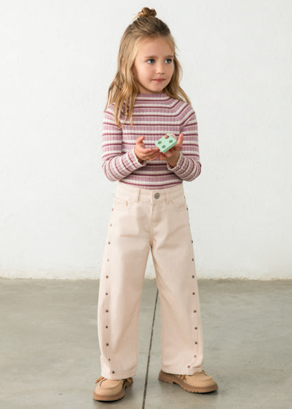 Young girl wearing a striped shirt and beige pants holding a toy against a white background