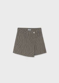 A pair of high-waisted, asymmetrical denim shorts in a muted olive green with a zebra-stripe pattern, featuring a button closure and front pockets, shown flat on a light gray background.
