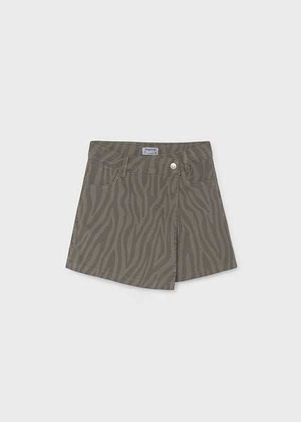 A pair of high-waisted, asymmetrical denim shorts in a muted olive green with a zebra-stripe pattern, featuring a button closure and front pockets, shown flat on a light gray background.
