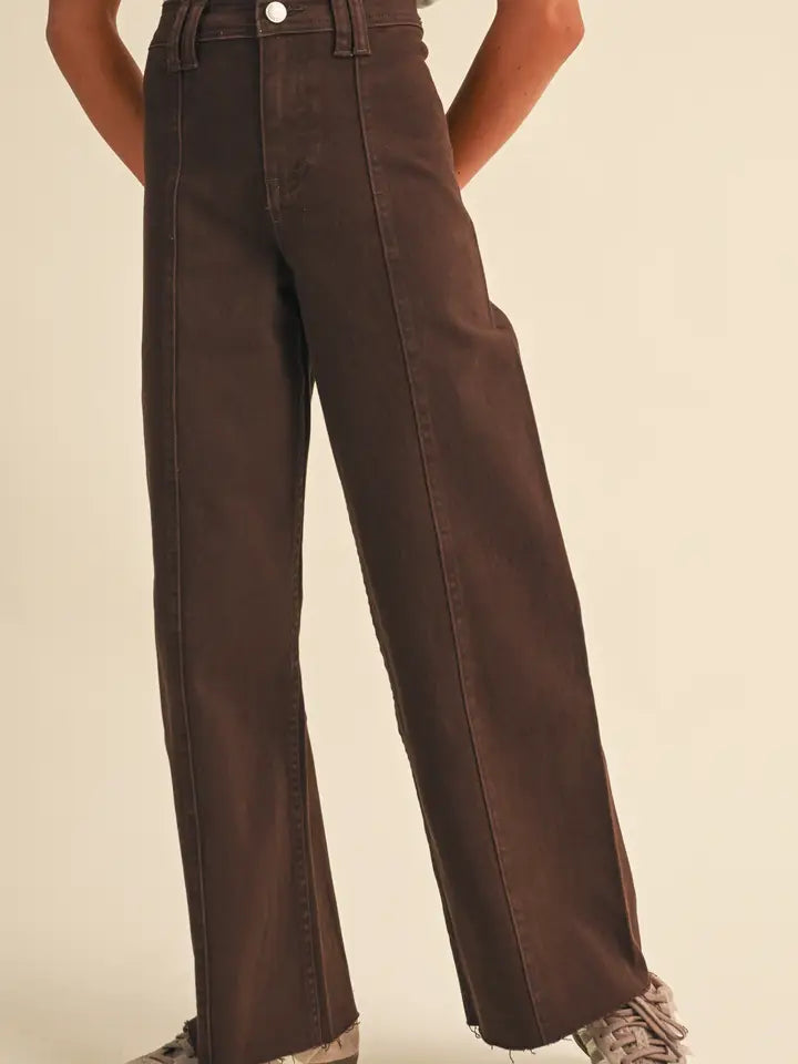 A person wearing dark brown wide-leg jeans with a high waist, shown from the waist down against a plain beige studio background.