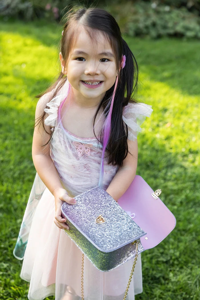 Young girl holding a sparkly handbag in a grassy outdoor setting
