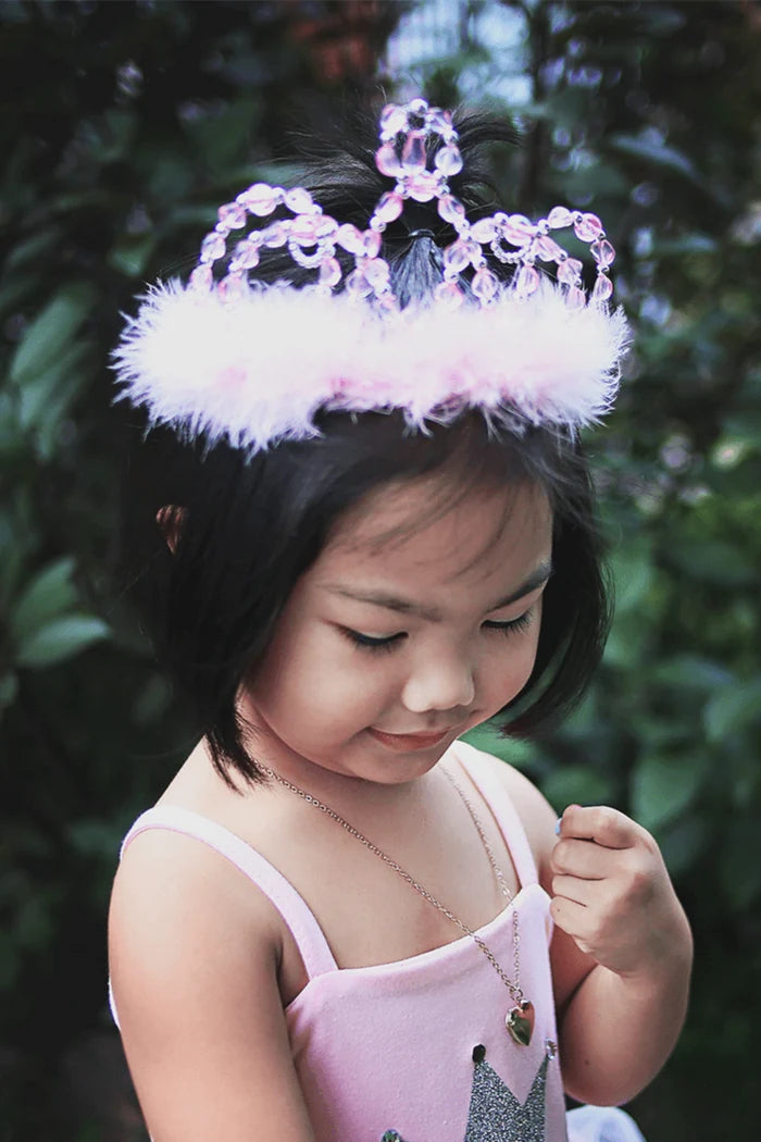 Young girl wearing a pink tiara with feathers against a blurred green background
