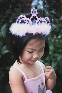 Young girl wearing a pink tiara with feathers against a blurred green background