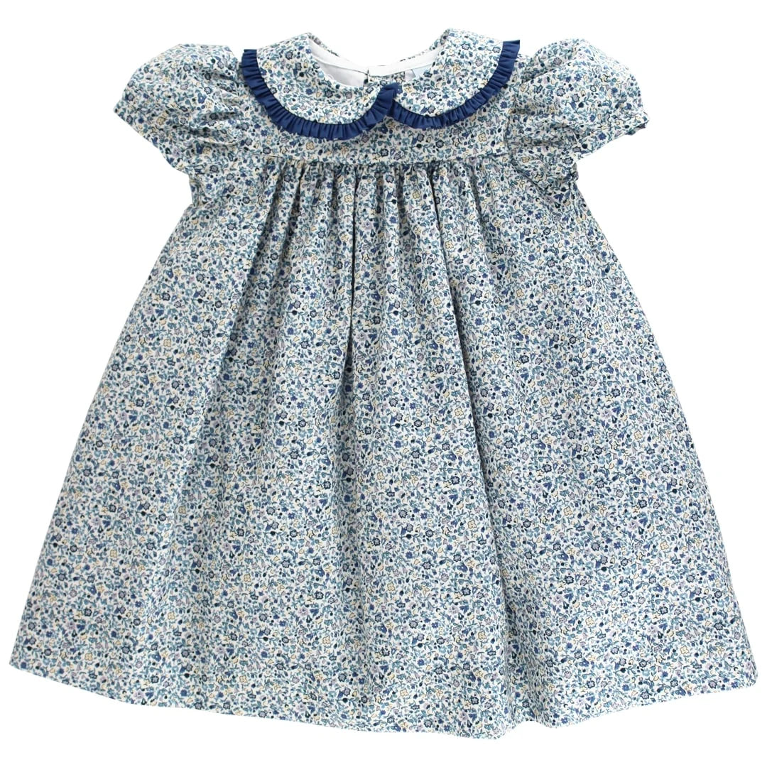 A baby girl's smocked dress featuring a blue and white floral print, with a navy blue Peter Pan collar and ruffled short sleeves, shown against a plain white background.