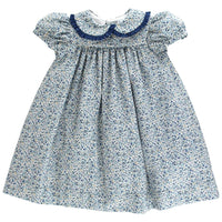 A baby girl's smocked dress featuring a blue and white floral print, with a navy blue Peter Pan collar and ruffled short sleeves, shown against a plain white background.