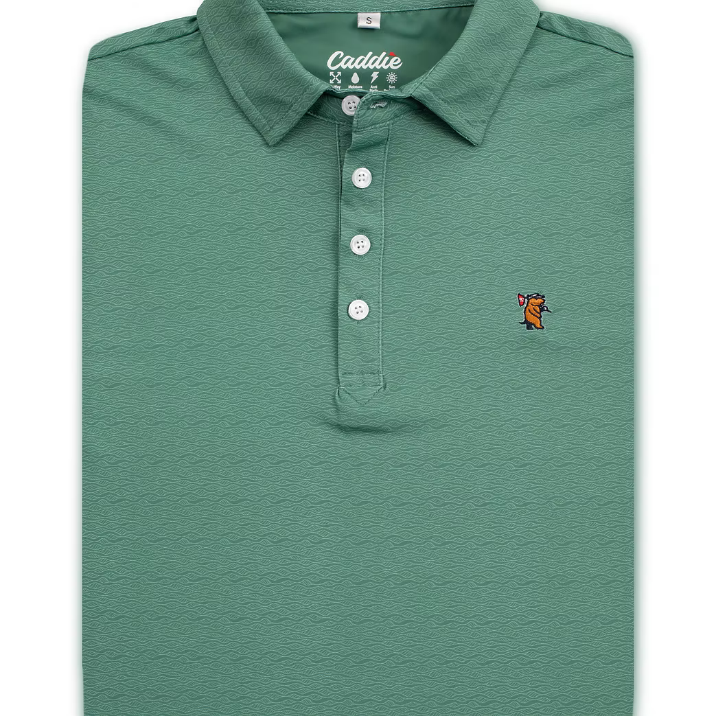 A folded sage green polo shirt with a textured wavy pattern, featuring a white button placket and a small embroidered fox logo on the left chest.