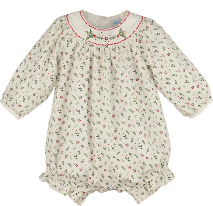 A baby long-sleeve romper in cream cotton fabric with a small green and red floral print, featuring a smocked neckline with red trim and green floral embroidery.