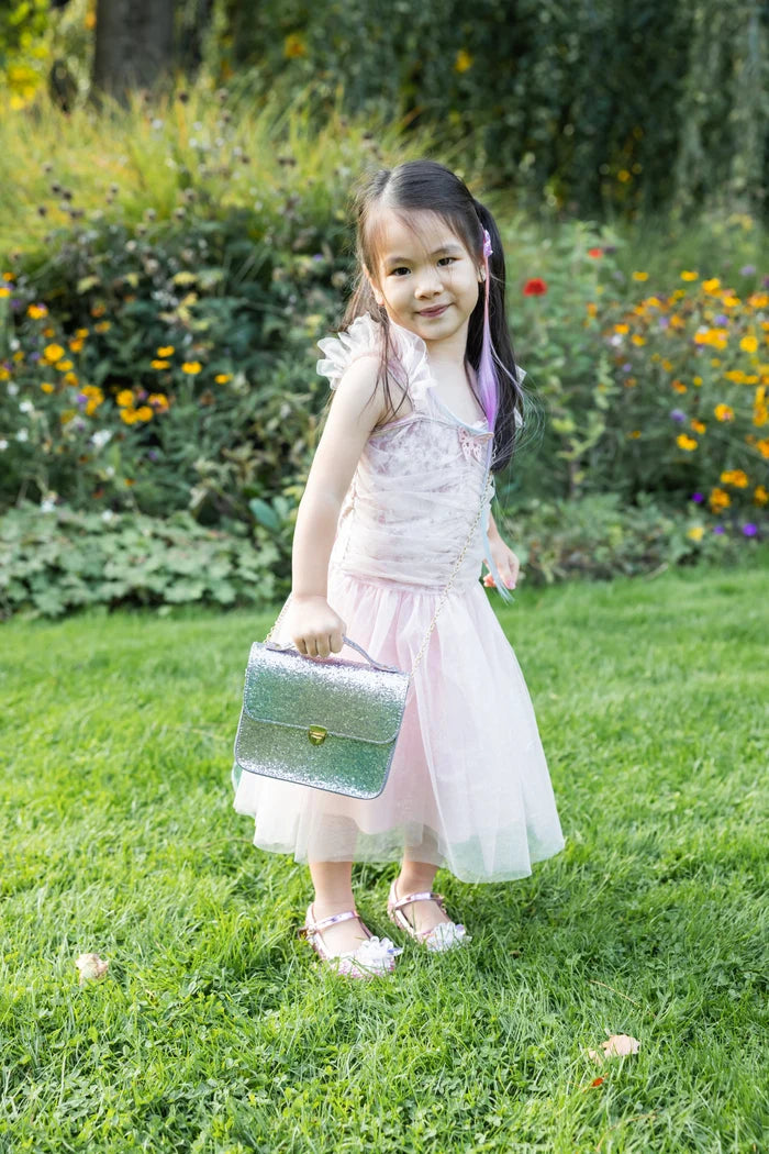 Young girl in a pink dress holding a silver suitcase in a garden setting
