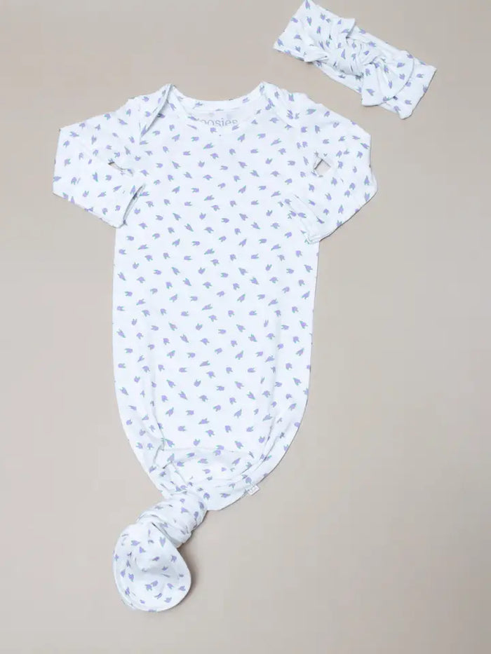 A baby outfit set featuring a short-sleeve knotted bodysuit and a matching headband, both in white with a light blue leaf print, laid flat on a neutral beige background.