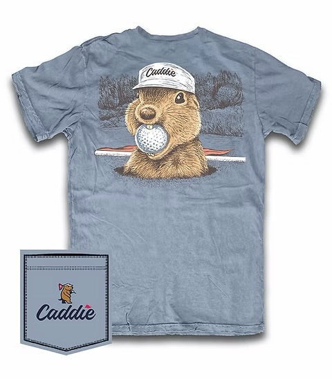 A light blue-gray short-sleeve t-shirt featuring a graphic of a brown groundhog wearing a white 'Caddie' cap and holding a golf ball. A matching 'Caddie' branded pocket graphic is shown in the bottom-left corner against a white background.