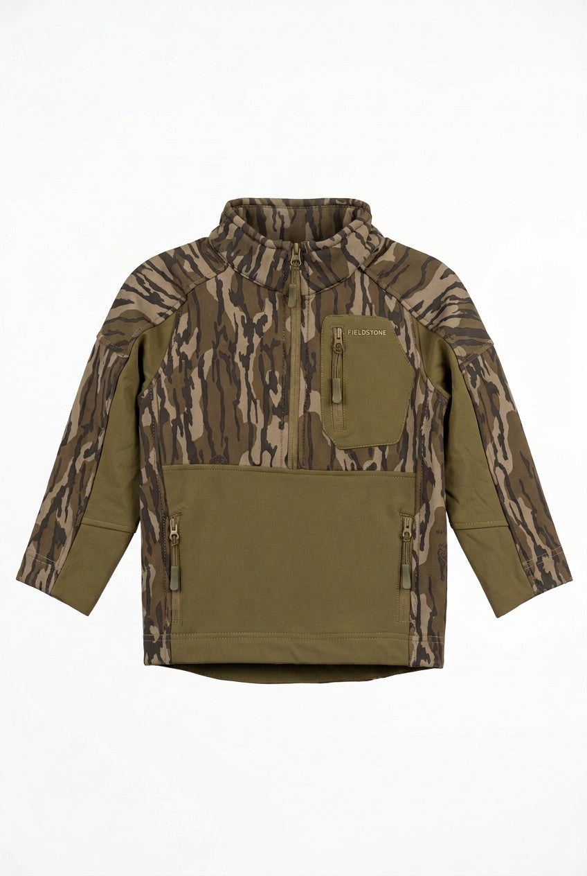 A camouflage hunting jacket with olive green panels and pockets, displayed on a hanger in a warehouse or retail setting with boxes stacked in the background.
