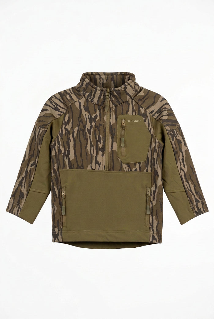 A camouflage hunting jacket with olive green panels and pockets, displayed on a hanger in a warehouse or retail setting with boxes stacked in the background.