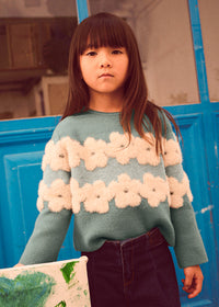 Young girl wearing a floral sweater in front of a blue door.