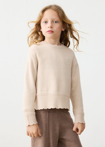 Young girl wearing a beige sweater and brown pants on a white background