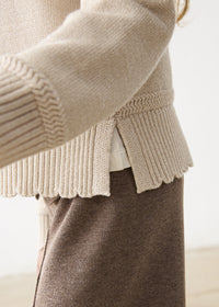 Close-up of a person wearing a beige knit cardigan and brown pants.