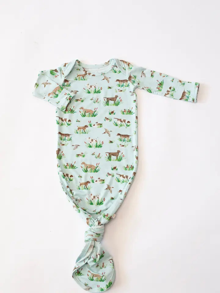 A baby long-sleeve bodysuit with a knotted crotch, featuring an all-over print of deer, rabbits, and grass on a pale mint green background, laid flat on a white surface.