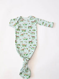 A baby long-sleeve bodysuit with a knotted crotch, featuring an all-over print of deer, rabbits, and grass on a pale mint green background, laid flat on a white surface.