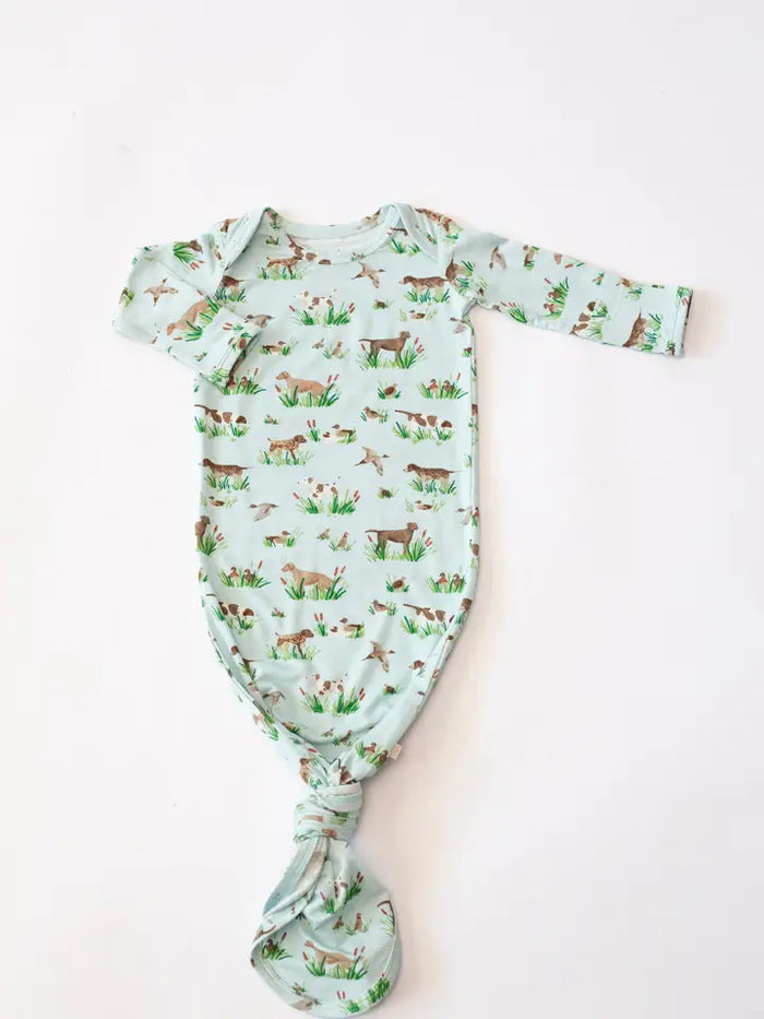 A baby long-sleeve bodysuit with a knotted crotch, featuring an all-over print of deer, rabbits, and grass on a pale mint green background, laid flat on a white surface.