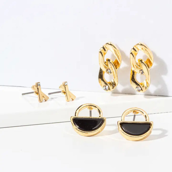 Three pairs of gold-toned earrings displayed on a clean white surface: small stud earrings, chain-link drop earrings with clear stones, and semi-circular dome earrings with black centers.