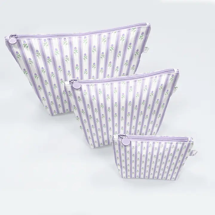 Three lavender and white striped zippered pouches with a small floral print, arranged by size on a light gray background.