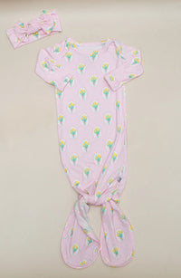 A baby footie sleeper in light pink with a repeating tulip print, shown with a matching pink bow headband on a light beige background.
