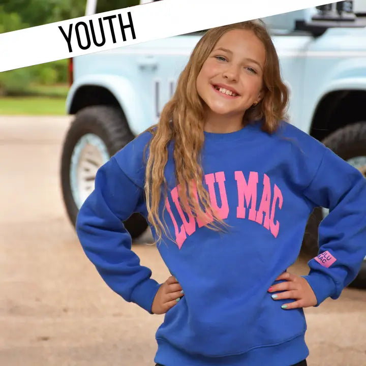 Girl wearing a blue sweatshirt with pink text, standing in front of a truck.