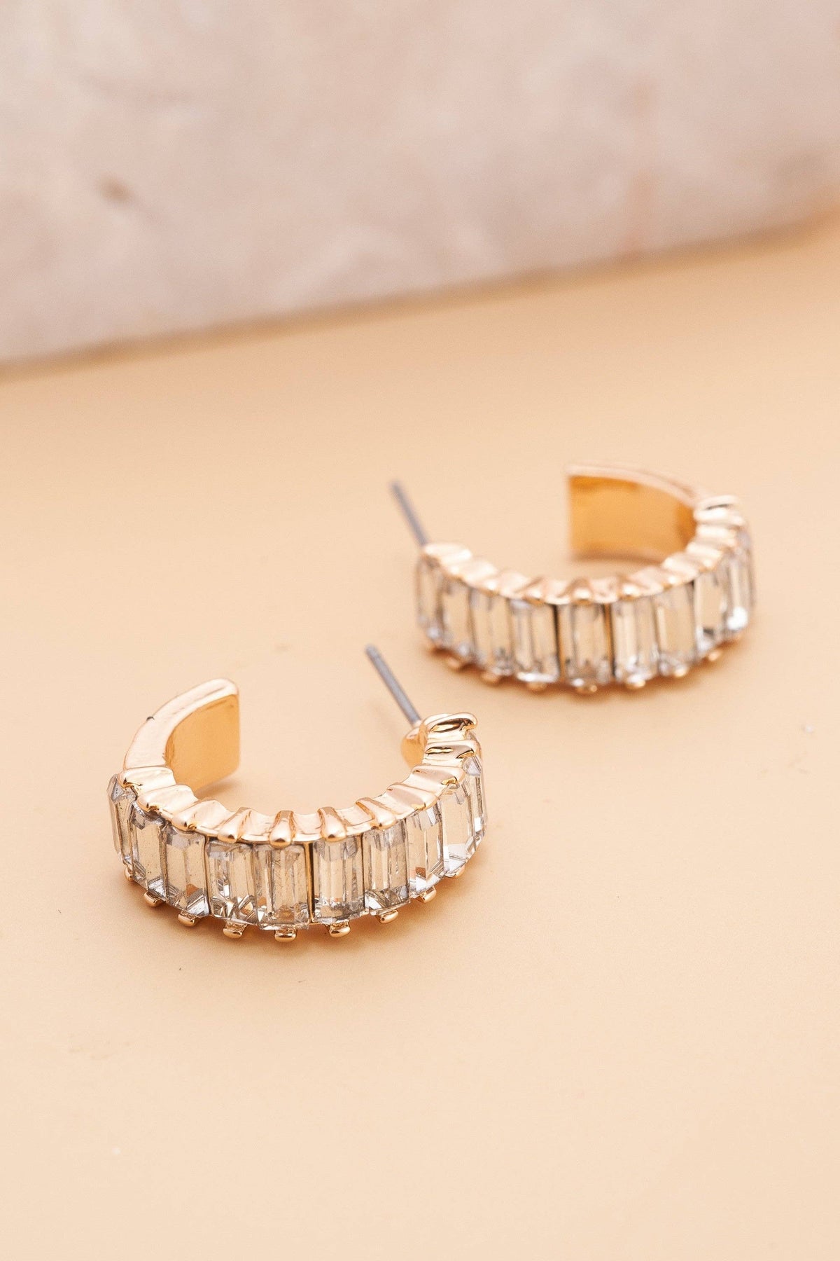 Gold hoop earrings with clear gemstones on a beige background