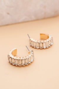 Gold hoop earrings with clear gemstones on a beige background